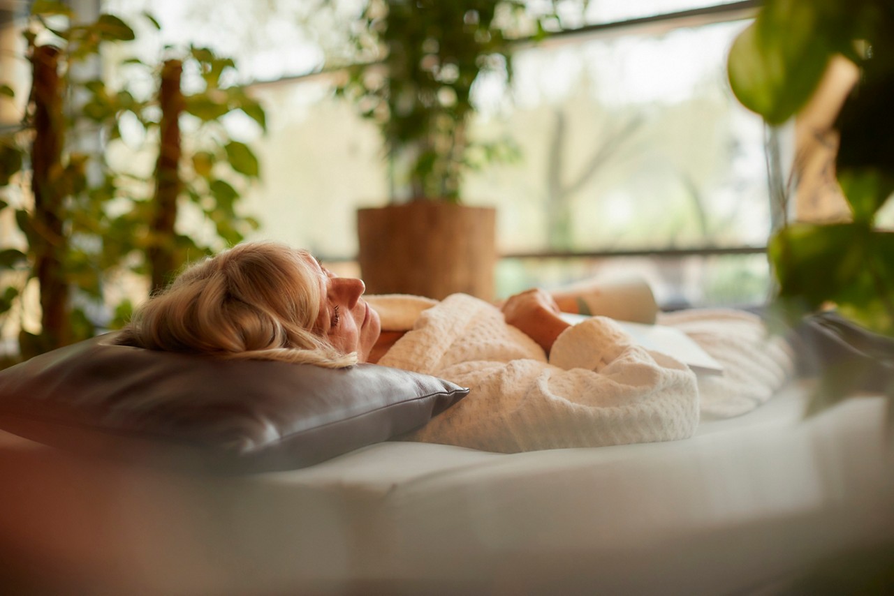 Lady laid back on a Waterbed in a serene area with lots of plants and natural lighting.